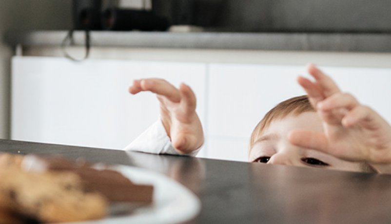Barn rækker ud efter chokolademad på køkkenbord