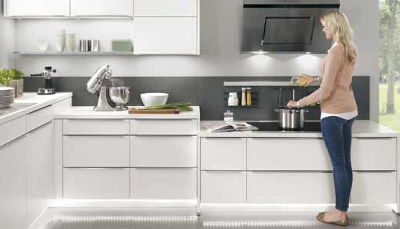 Kvinde står i hvidt luksus køkken med hvidevarer og bordplade